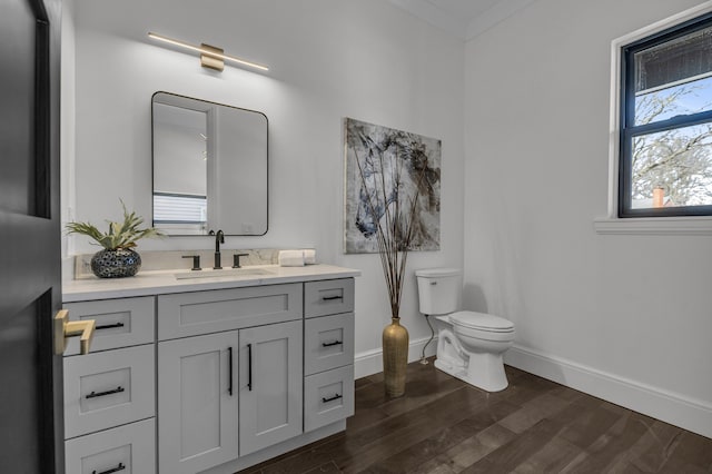 half bath with vanity, toilet, wood finished floors, and baseboards