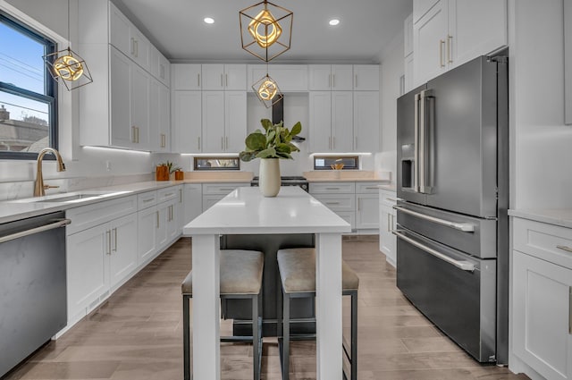 kitchen featuring a sink, stainless steel appliances, hanging light fixtures, and white cabinetry