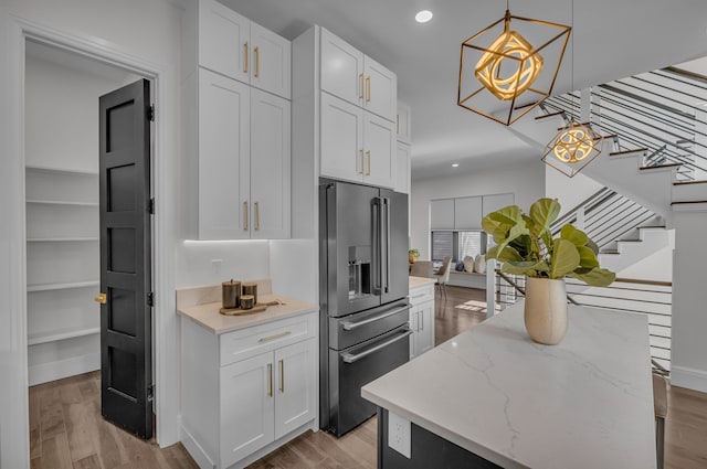 kitchen with white cabinets, light stone counters, high end fridge, and light wood-type flooring