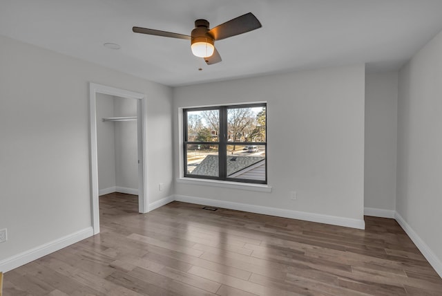 unfurnished bedroom featuring a walk in closet, wood finished floors, baseboards, and a closet