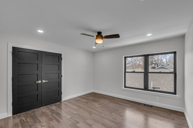 unfurnished room with wood finished floors, a ceiling fan, visible vents, and baseboards