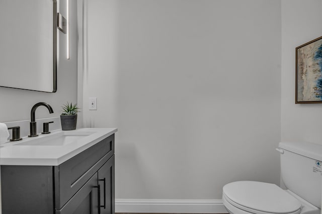 half bathroom featuring vanity, toilet, and baseboards