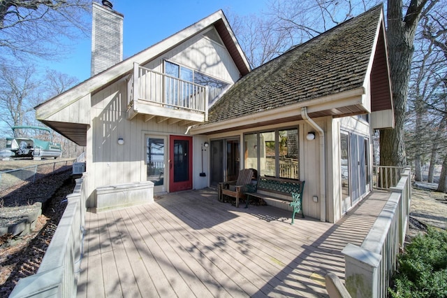 back of property featuring a wooden deck, fence, a balcony, and a chimney
