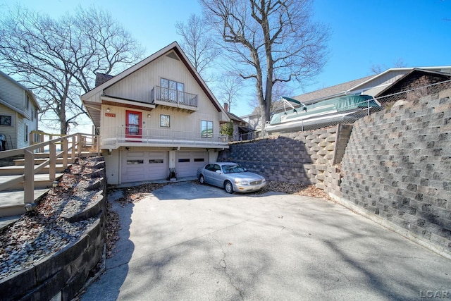 exterior space featuring concrete driveway, a balcony, an attached garage, and fence