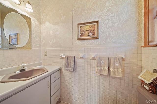 bathroom featuring wallpapered walls, tile walls, vanity, and a wainscoted wall