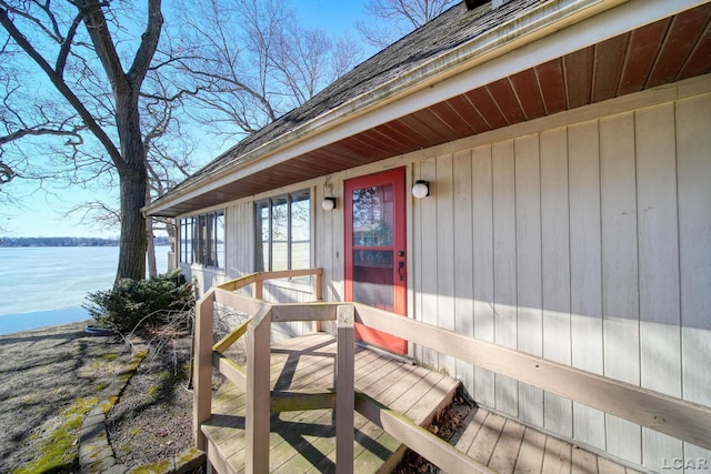 view of exterior entry with a shingled roof and a water view