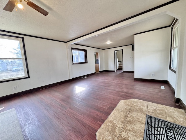 spare room featuring a ceiling fan, baseboards, dark wood-type flooring, a textured ceiling, and crown molding