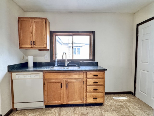 kitchen with dark countertops, a sink, brown cabinets, and white dishwasher