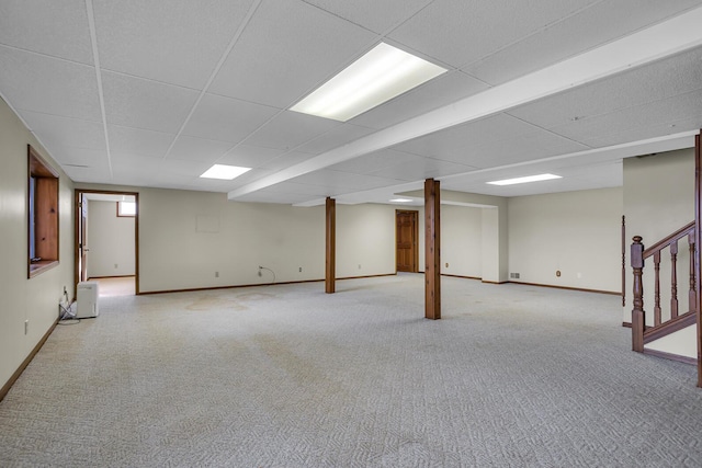 finished basement with a drop ceiling, baseboards, light colored carpet, and stairs