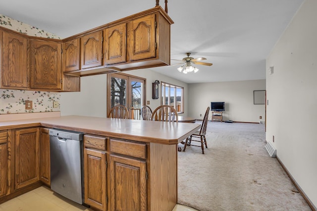 kitchen featuring stainless steel dishwasher, a peninsula, brown cabinets, and light carpet