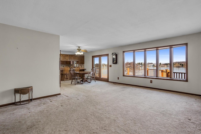 unfurnished living room with a ceiling fan, baseboards, a water view, and light carpet