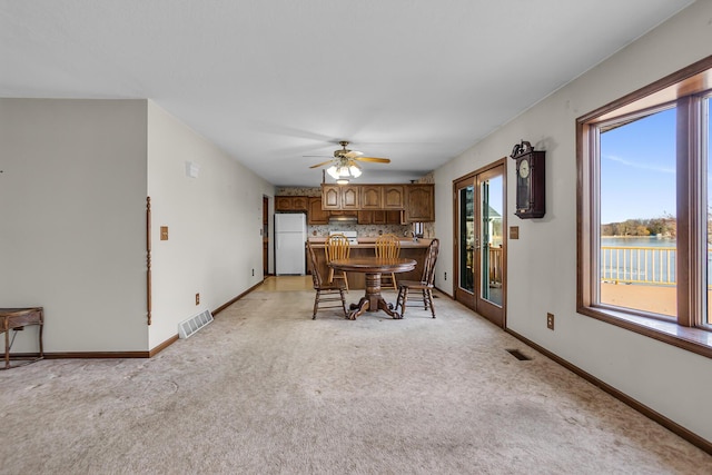 dining room with visible vents, baseboards, light colored carpet, and a ceiling fan