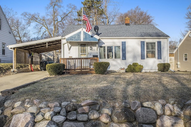 view of front of home with a shingled roof, a carport, driveway, and a chimney