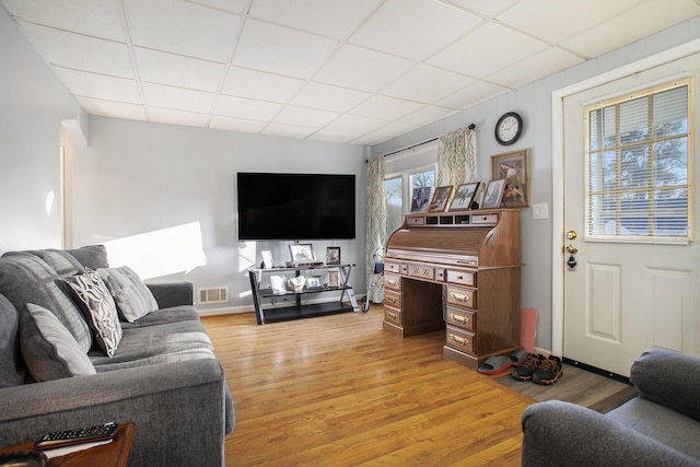 living room featuring visible vents, light wood-type flooring, a drop ceiling, and baseboards