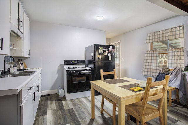 kitchen with wood finished floors, white cabinetry, freestanding refrigerator, a sink, and range with gas cooktop