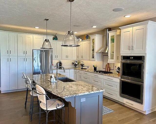 kitchen featuring wall chimney range hood, appliances with stainless steel finishes, wood finished floors, white cabinetry, and a sink