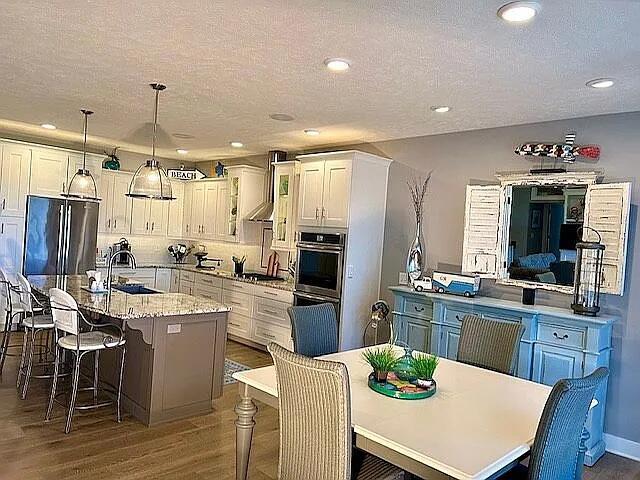 kitchen featuring a breakfast bar area, an island with sink, wood finished floors, fridge, and a sink