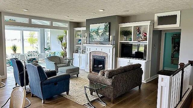 living area featuring wood finished floors, a textured ceiling, and a glass covered fireplace