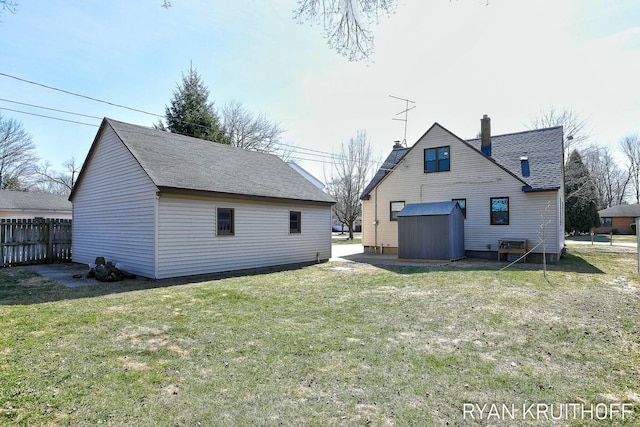 rear view of house featuring an outbuilding, a chimney, a lawn, and fence