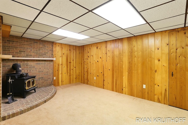 finished below grade area with a paneled ceiling, wooden walls, carpet, and a wood stove