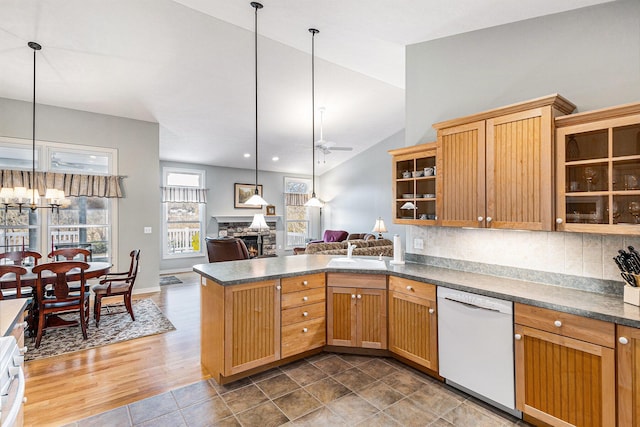 kitchen with dark countertops, a stone fireplace, ceiling fan with notable chandelier, and white dishwasher