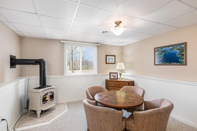 sitting room featuring carpet, baseboards, visible vents, a wood stove, and a paneled ceiling