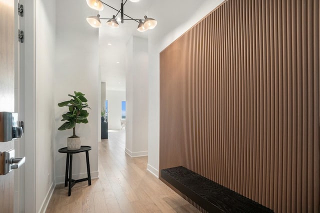 corridor featuring light wood-type flooring, baseboards, and an inviting chandelier