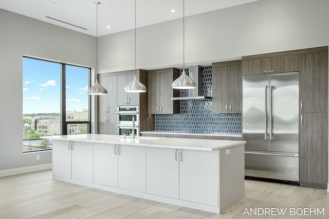 kitchen featuring a large island, stainless steel appliances, light wood-style floors, and wall chimney range hood