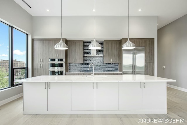 kitchen featuring a large island, modern cabinets, a sink, stainless steel appliances, and wall chimney exhaust hood