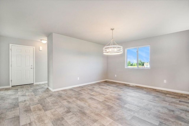 empty room with light wood-type flooring, baseboards, and a chandelier