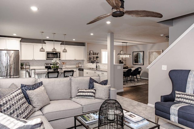 living room with recessed lighting, ceiling fan with notable chandelier, baseboards, and dark wood-style flooring