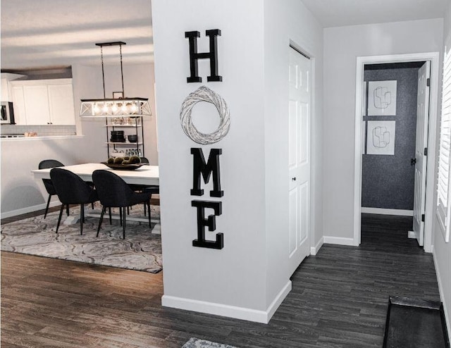 hall featuring dark wood finished floors, a notable chandelier, and baseboards