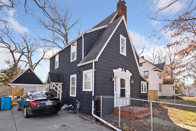 view of front facade with a detached garage, roof with shingles, a chimney, and fence