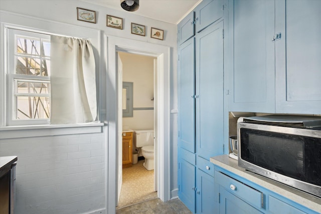 kitchen featuring blue cabinetry, stainless steel microwave, tile walls, and a healthy amount of sunlight