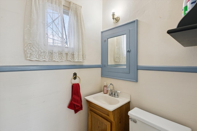 half bath featuring vanity, toilet, tile walls, and wainscoting