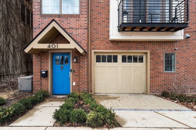 entrance to property featuring decorative driveway, an attached garage, and brick siding