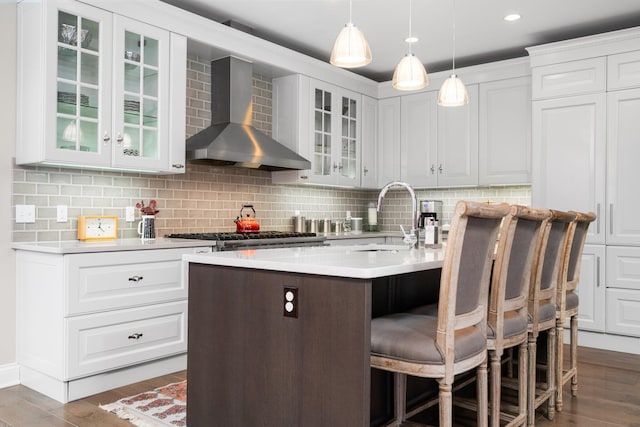 kitchen featuring a breakfast bar, light countertops, wood finished floors, wall chimney exhaust hood, and a sink