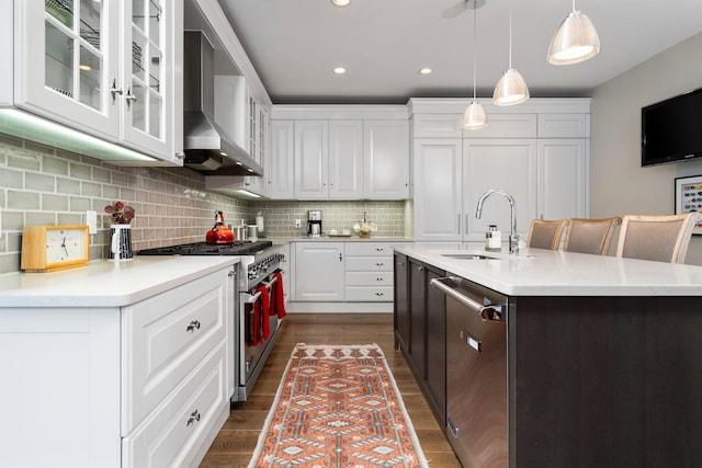 kitchen featuring a sink, stainless steel appliances, light countertops, wall chimney range hood, and backsplash