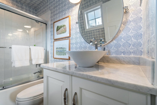 bathroom featuring wallpapered walls, toilet, vanity, and bath / shower combo with glass door