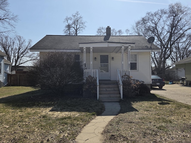 bungalow with a porch, fence, a front yard, a shingled roof, and a chimney