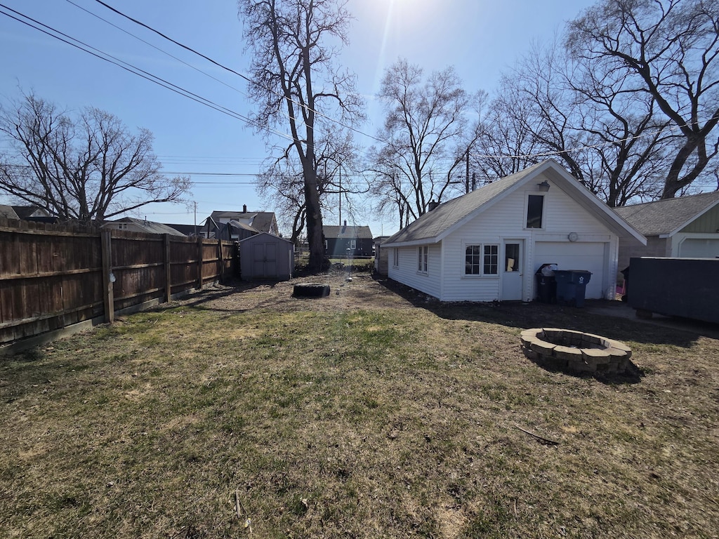 view of yard featuring an outbuilding, fence, a shed, a fire pit, and a garage