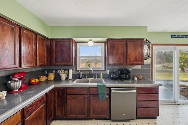 kitchen featuring a sink, backsplash, light floors, dishwasher, and tile counters