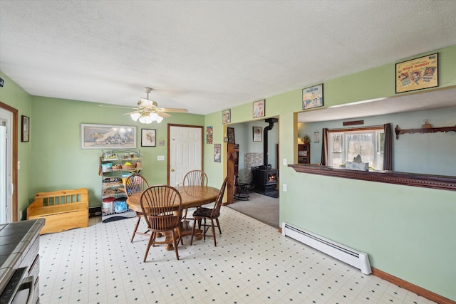 dining area featuring a ceiling fan, a textured ceiling, baseboards, baseboard heating, and a wood stove