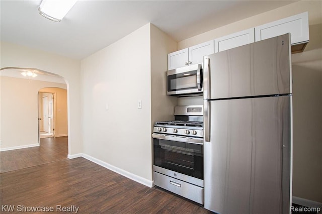 kitchen featuring baseboards, dark wood finished floors, stainless steel appliances, arched walkways, and white cabinetry