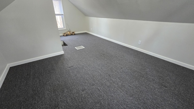 additional living space featuring visible vents, dark carpet, lofted ceiling, and baseboards