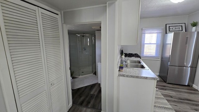 kitchen with light countertops, freestanding refrigerator, wood finished floors, white cabinets, and a sink