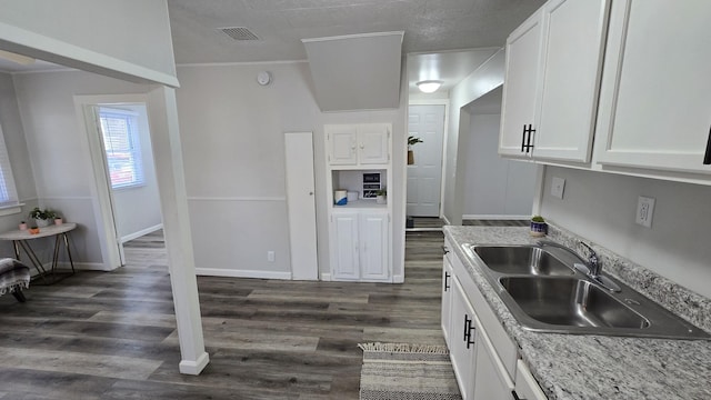 kitchen featuring visible vents, dark wood-type flooring, baseboards, white cabinets, and a sink