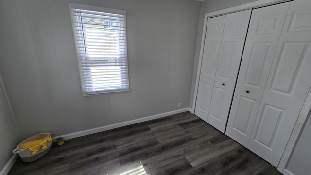 unfurnished bedroom with multiple windows, baseboards, dark wood-style flooring, and a closet