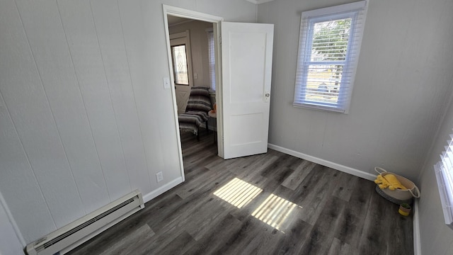 unfurnished bedroom with a baseboard heating unit, wood finished floors, and baseboards