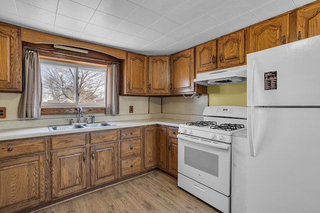 kitchen featuring under cabinet range hood, white appliances, brown cabinetry, and a sink